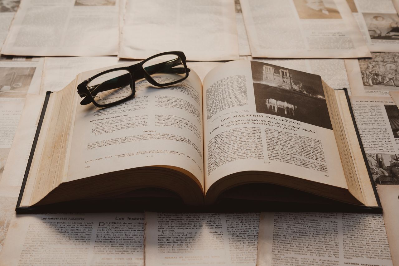 Offerings A vintage book open on a table, surrounded by old papers, with resting glasses.