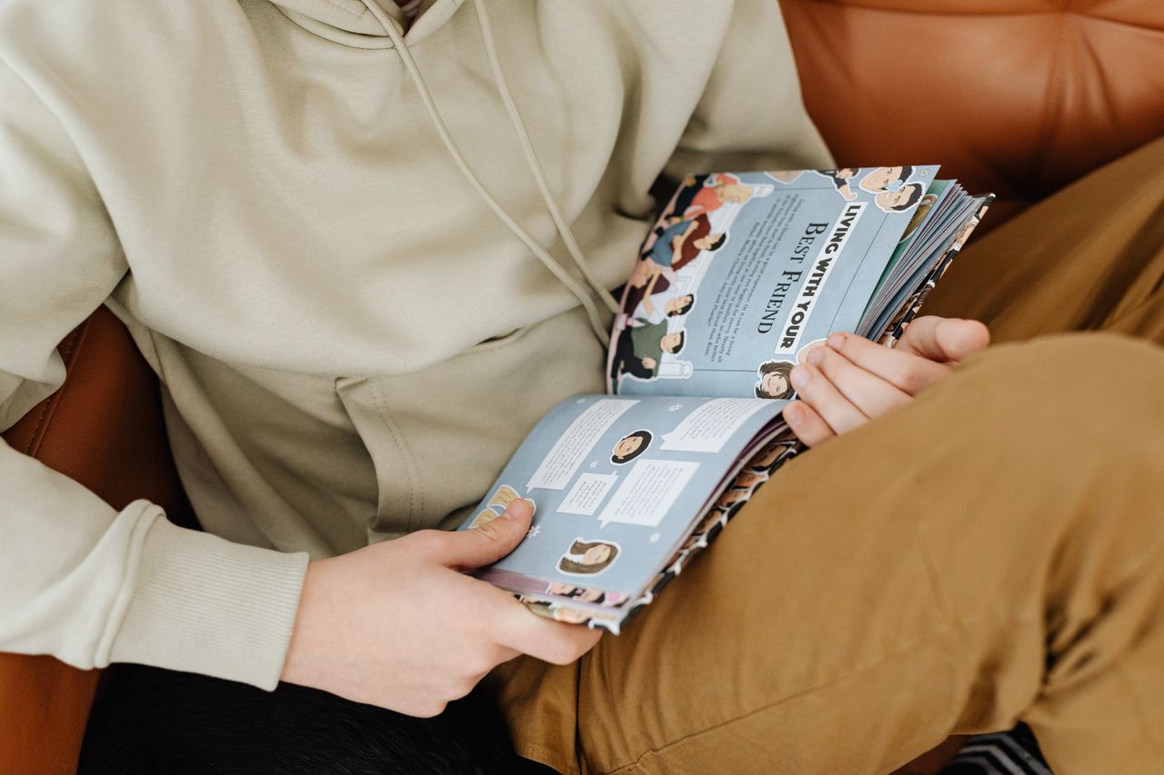 Offerings Close-up of a person reading a colorful illustrated book on a cozy living room couch.